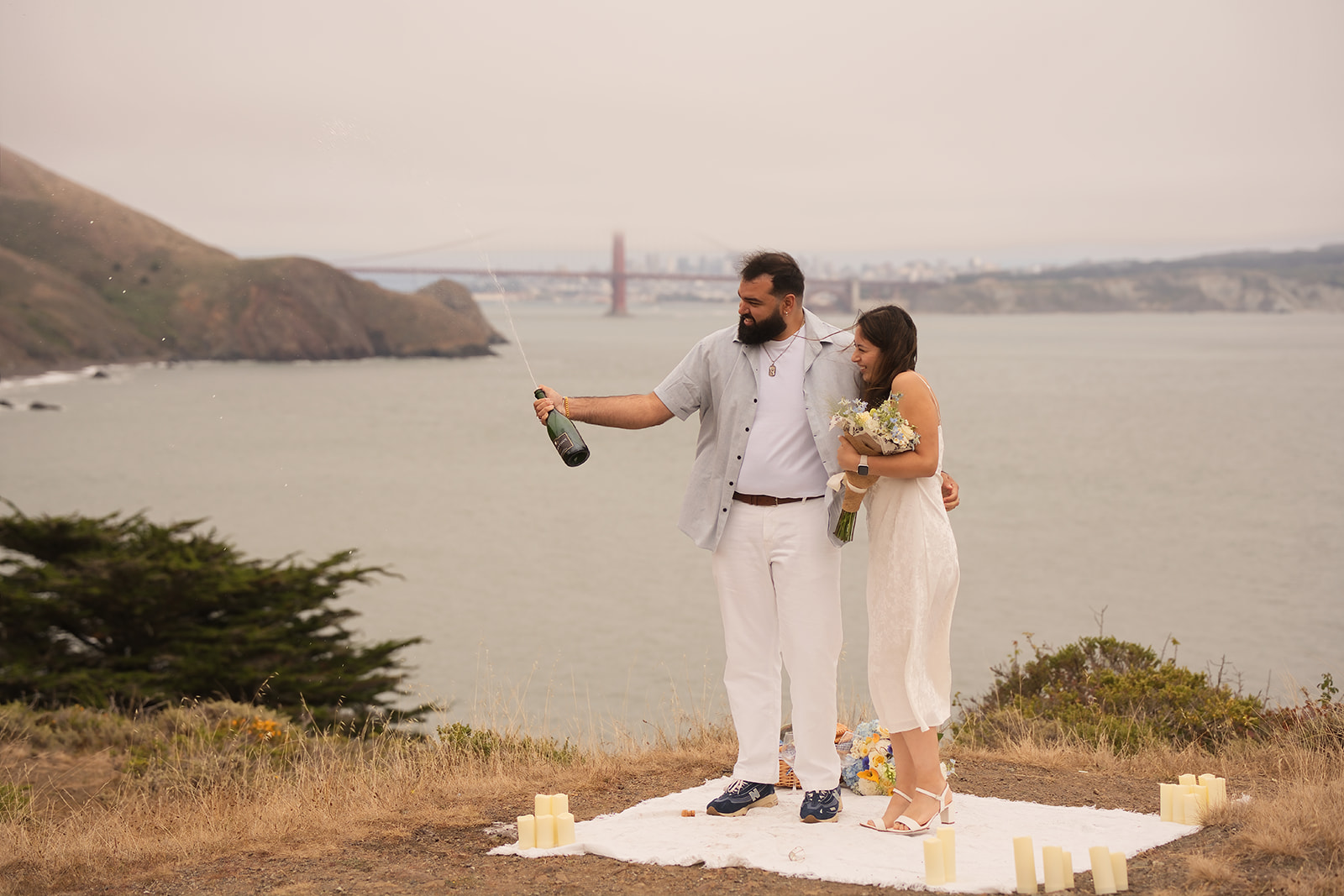 Couple celebrating their Golden Gate Bridge proposal with champagne and flowers