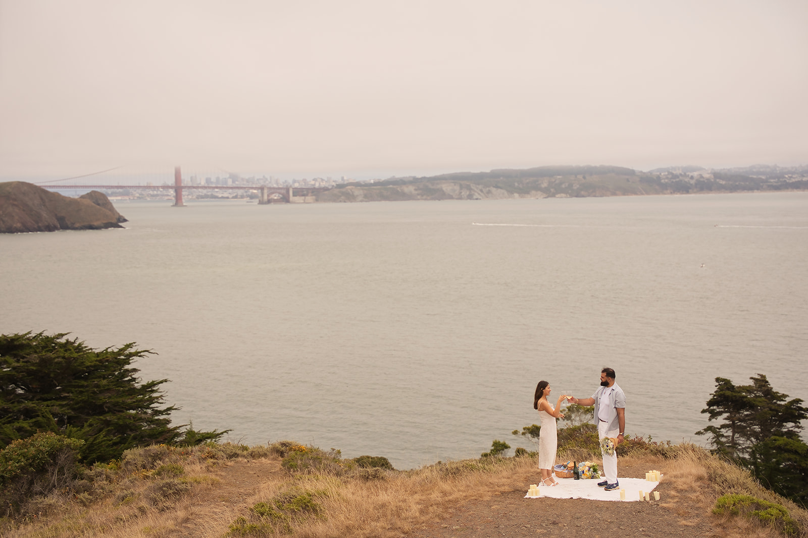 Wide view of a couple celebrating their proposal with the Golden Gate Bridge