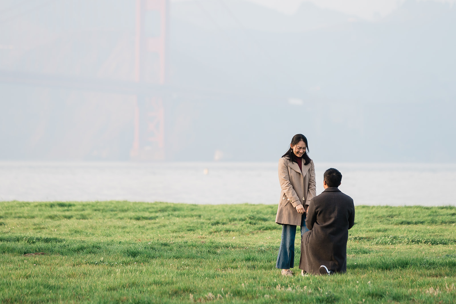 A couple celebrating their proposal at Chrissy Field with the Golden Gate Bridge behind them